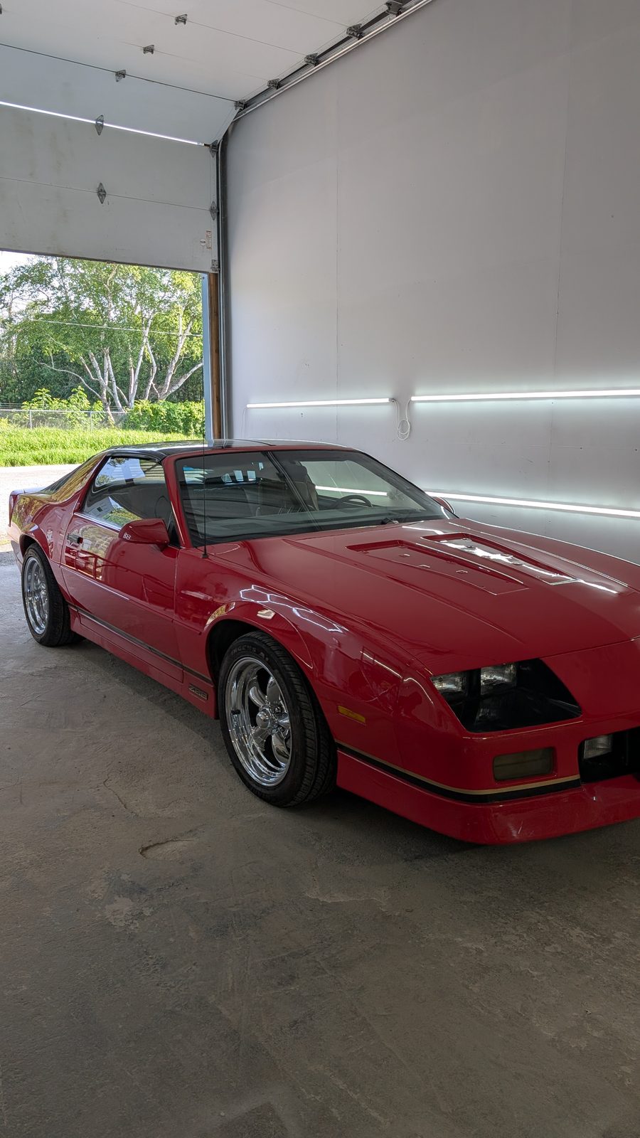 Reconditioned red 1980s Camaro with a deep gloss finish in the shop bay